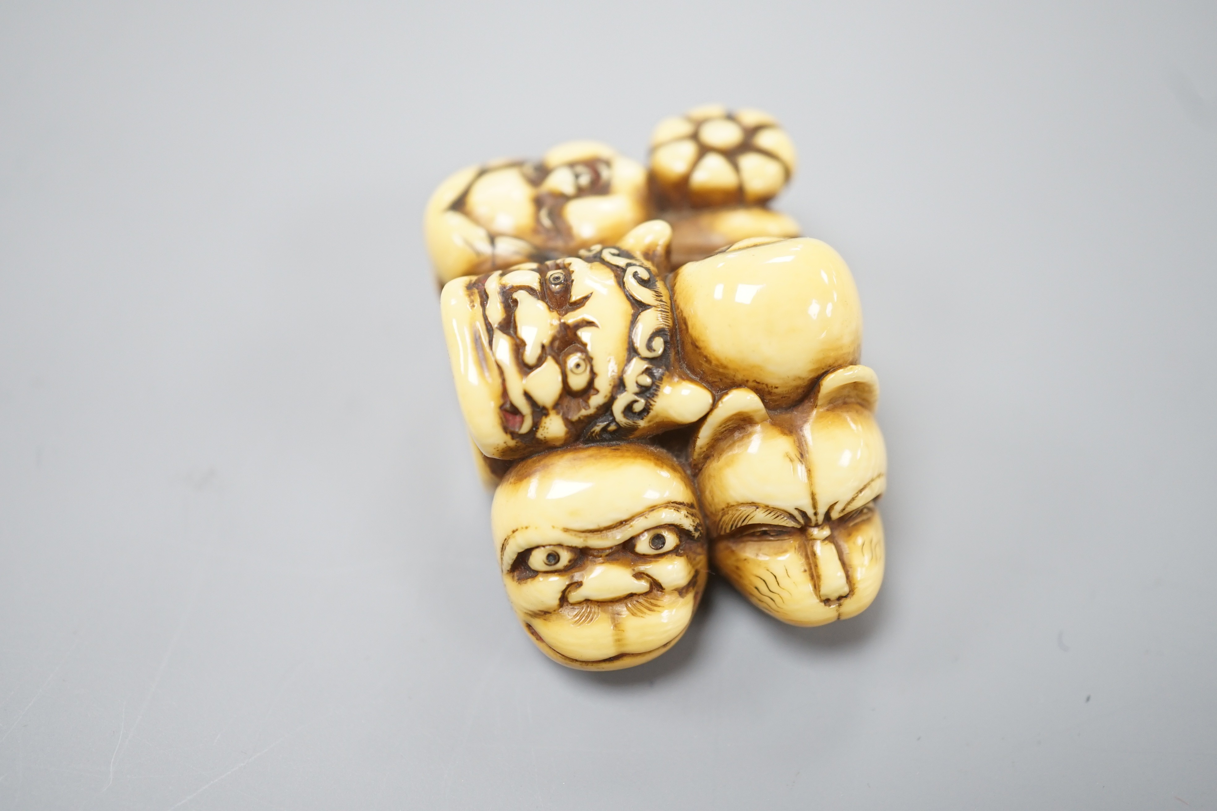 A Japanese ivory netsuke of a Daruma doll and four noh masks, signed, 19th century, 3.8cm